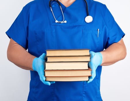 doctor in blue uniform and sterile latex gloves holds a stack of books in his hand photo