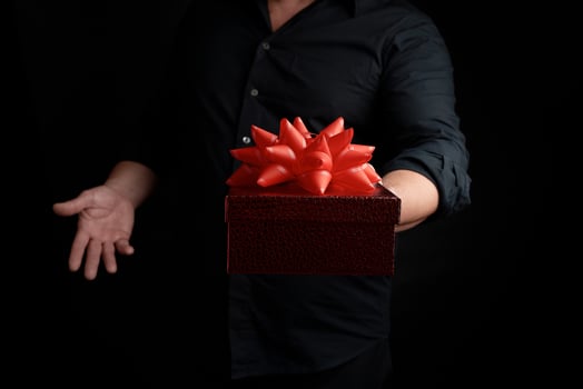adult man in a black shirt holds a red square box with a knotted bow on a dark background photo