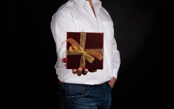 adult man in a white shirt holds a red square box with a knotted golden bow photo