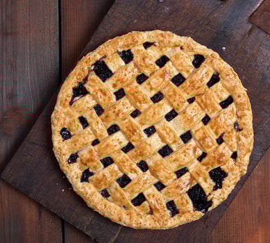 baked whole black currant pie lay on a brown wooden cutting board photo