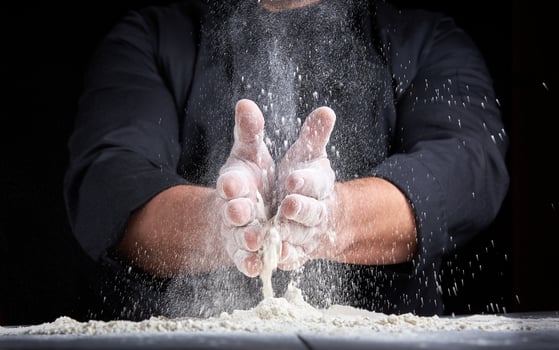 chef in black uniform pours white wheat flour out of his hands photo