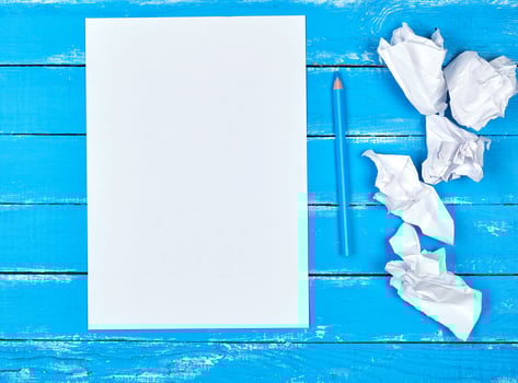 blank white rectangular sheet of paper and crumpled pieces of paper on a blue wooden background photo