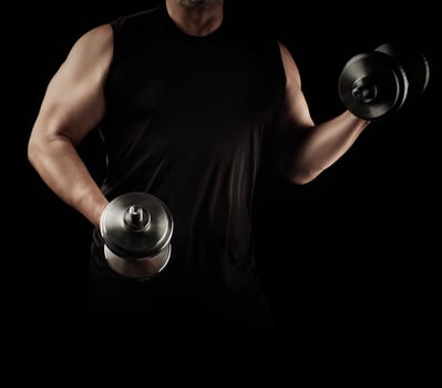 man in black clothes holds steel dumbbells in his hands, his muscles are tense photo