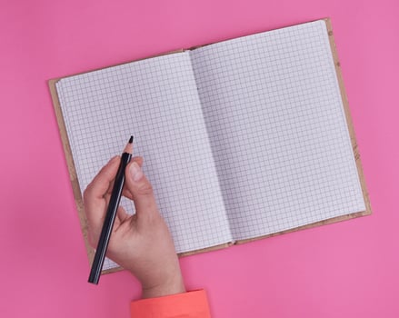 open notebook in a cell and a female hand holding a black wooden pencil photo