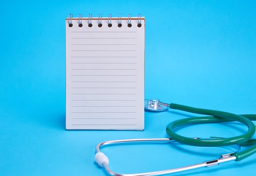 green medical stethoscope and empty paper notebook photo