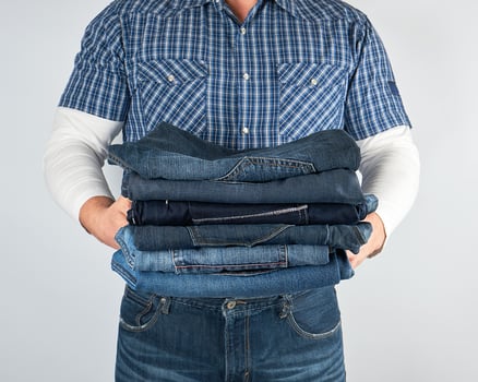 man in jeans and blue plaid shirt holding a pile of jeans photo