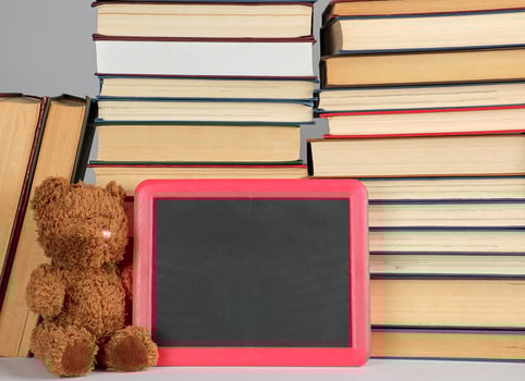 brown teddy bear and empty black board in red frame on the background of pile of books photo