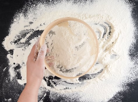women's hands hold a round wooden sieve and sift white wheat flour photo
