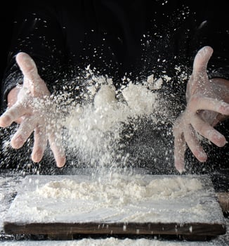chef in black uniform sprinkles white wheat flour over the table photo