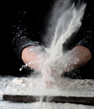 chef in black uniform sprinkles white wheat flour in different directions photo