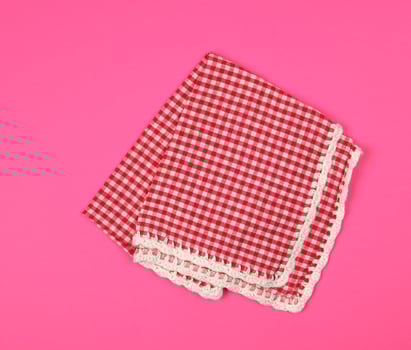 folded red kitchen towel in a cage on a pink background photo