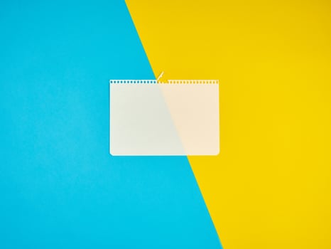 blank white sheet of paper torn from a notebook on a blue-yellow background photo