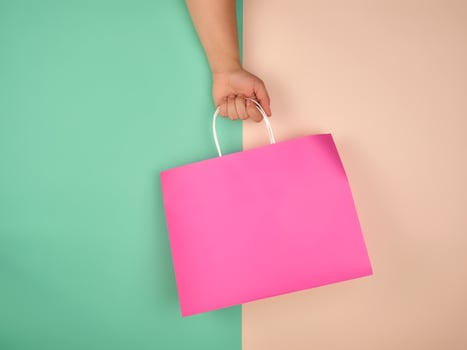 female hand holding a pink paper shopping bag on green beige background photo