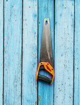 hand saw is hanging on a nail on a blue wooden wall photo