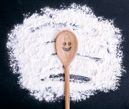 spoon with a carved smiling face lies on scattered flour photo