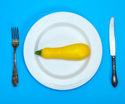 raw yellow squash in a white ceramic plate and iron fork with a knife photo