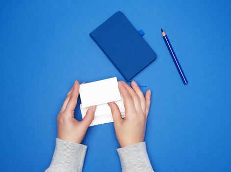 two female hands holding a stack of empty white paper business cards on a blue background photo