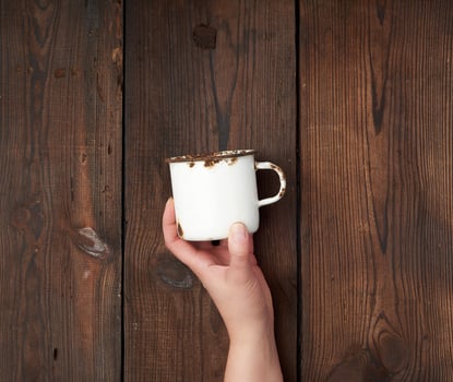 hand holds a white metal cup with rust on a brown wooden background photo