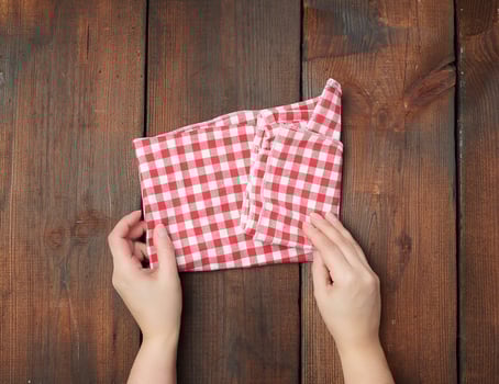 hands hold white red checkered kitchen towel on a brown wooden background photo