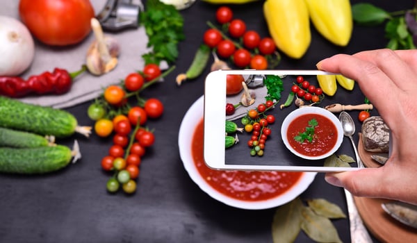 Female hand with smartphone in hand photographs soup gazpacho photo