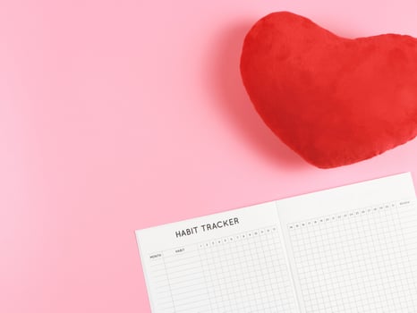 flat lay of habit tracker book with  red heart shape pillow on pink  background with copy space. photo