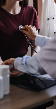 Homecare nursing service and elderly people cardiology healthcare. Close up of young hispanic female doctor nurse check mature caucasian man patient heartbeat using stethoscope during visit photo