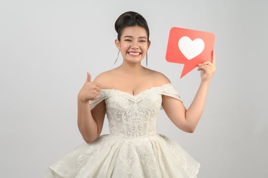 Asian beautiful bride smiling and posing with heart sign on white background photo