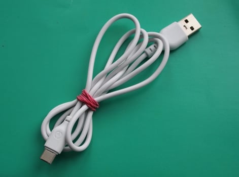 A white Micro USB cable, has a wide and flat shape for transferring data and charging smartphone batteries. Illustration of a roll of a micro USB cable on a wooden table. photo