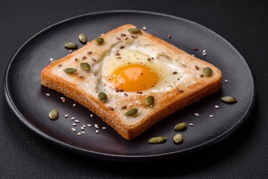Heart shaped fried egg in bread toast with sesame seeds, flax seeds and pumpkin seeds on a black plate photo