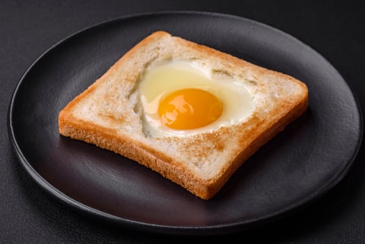Heart shaped fried egg in bread toast with sesame seeds, flax seeds and pumpkin seeds on a black plate photo
