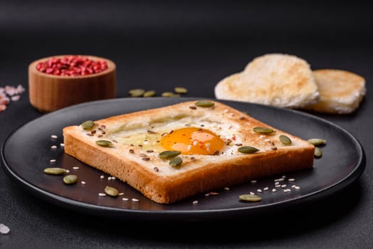 Heart shaped fried egg in bread toast with sesame seeds, flax seeds and pumpkin seeds on a black plate photo