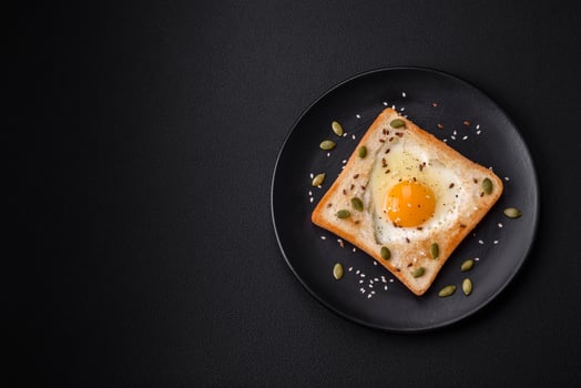 Heart shaped fried egg in bread toast with sesame seeds, flax seeds and pumpkin seeds on a black plate photo