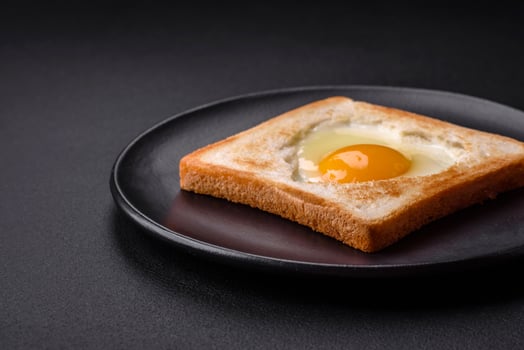 Heart shaped fried egg in bread toast with sesame seeds, flax seeds and pumpkin seeds on a black plate photo