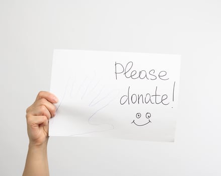 female hand holding a piece of paper with the inscription please donate photo