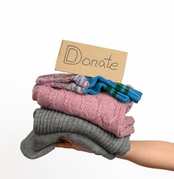 female hand holding a stack of clothes, help and volunteering concept, donation photo