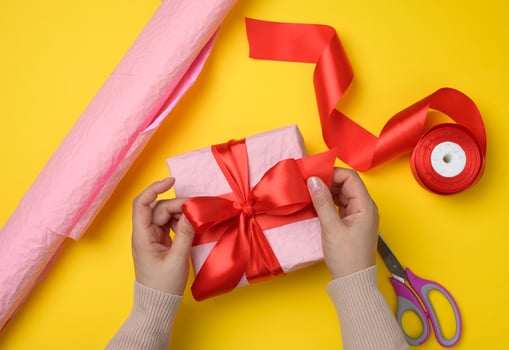 female hands tie a silk ribbon on a wrapped box in pink paper. photo