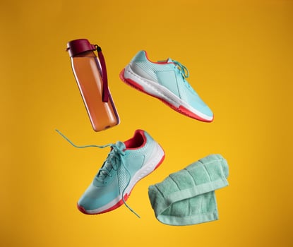 pink plastic water bottle and green towel and pair of textile blue sneakers with laces levitate on a yellow background photo
