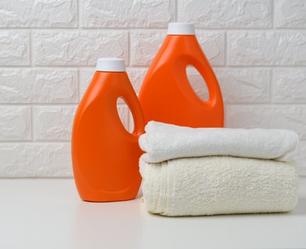 orange plastic bottle of liquid washing powder and folded towels on a white shelf photo