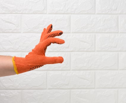 female hand in an orange work protective glove against the background of a white brick wall, the hand conditionally holds an object photo