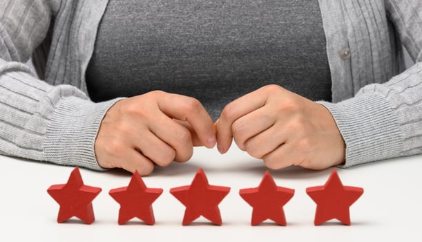 Customer experience feedback concept. Five red stars, the best rating of excellent services with a female hand to meet. White table photo