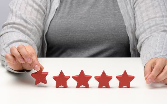 Customer experience feedback concept. Five red stars, the best rating of excellent services with a female hand to meet. White table photo