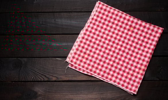 folded red and white cotton kitchen napkin on a wooden brown background, top view, copy space photo