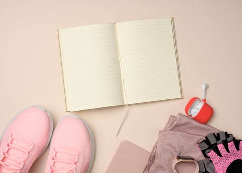 open notebook with blank pages, pink sneakers and smart gadgets on a beige background. Place to record goals and achievements, schedule photo