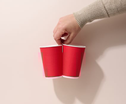 hand holds paper cardboard red cups for coffee, beige background. Eco-friendly tableware, zero waste photo