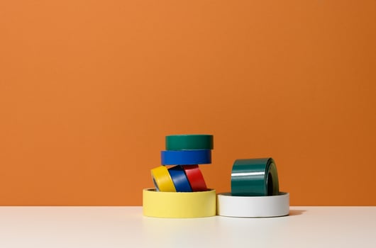 various skeins of multicolored scotch tape and electrical tape onorange background, copy space photo