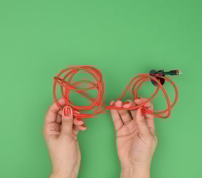female hand holds twisted cable for charging mobile devices in a red textile wrapper on a green background photo