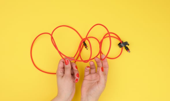 female hand holds twisted cable for charging mobile devices in a red textile wrapper on a yellow background photo