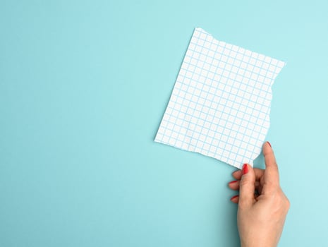 female hand holding a torn blank sheet of paper in a cage on a blue background photo