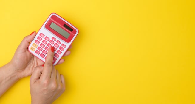 female hand holding a pink calculator on a yellow background, copy space photo
