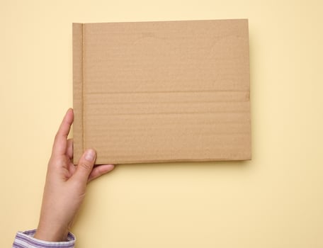 male hand hold a blank torn piece of brown paper, beige background photo